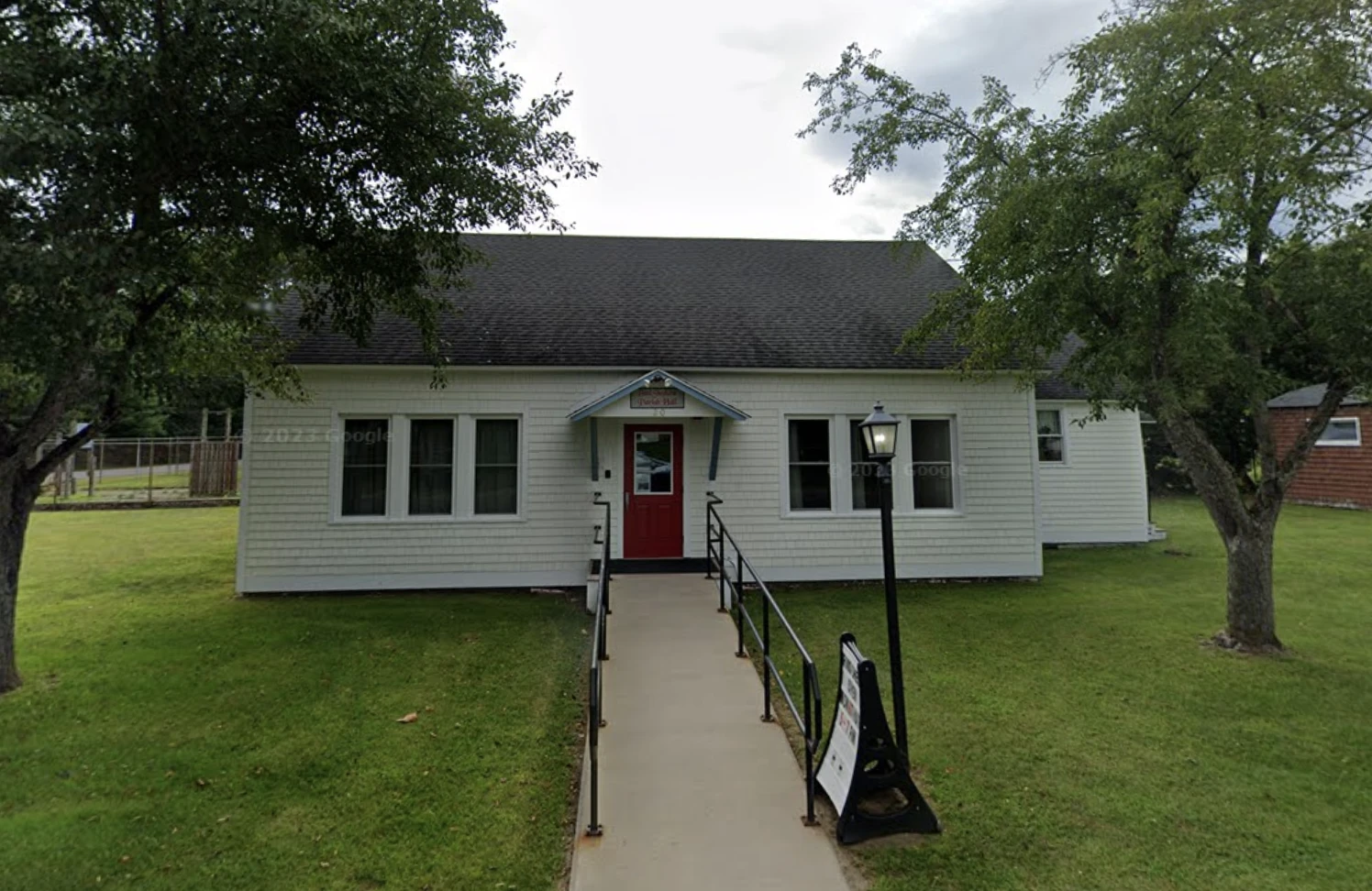 A simple, vinyl sided structure with concrete ramp to the red door